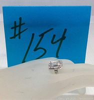 Ring shown on display hand with blue lot number card in background to establish identity and size.