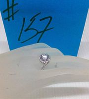 Front angle view of Swarovski zirconia round centre stone bypass ring on a display hand with a blue tag marked #157 visible in the background.