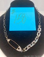 Necklace with safety pin pendant displayed on black jewelry bust with blue sticky note marked #158.