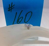 Ring displayed on white mannequin hand with blue #160 sign in background