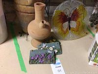 Close-up of ceramic jug, ceramic floral plaques with daisies and violets, and butterfly glass plate.
