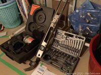 Photo showing a Black and Decker drill kit in case with drill bits, metal level, hammer, and assorted light bulbs packaged on the floor.