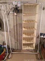 Photo of white metal clothes rack with beige cloth hanging organizer and assorted hangers