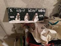 Wooden Warm Winter Welcome sign featuring three snowmen with a black background and snow at the bottom