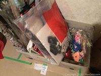 Clear plastic wheeled storage bin filled with gift bags, ribbons, and candles with some rolls of wrapping paper standing beside the bin.