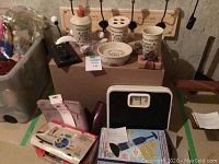 Bathroom accessories set labeled 'Paris' with soap dispenser, cup, toothbrush holder, soap dish, and other items. Also visible are bathroom scale and iron box.