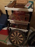Storage rack holding various board games and a dartboard on the bottom shelf.