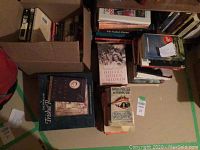 Photo showing multiple paperbacks and hardcover books arranged on a floor with visible titles.