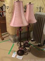 Two 32 inch tall table lamps with pink fabric shades and dark bronze metal bases with pink glass accents in basement setting.