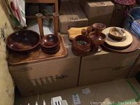 Photo showing assortment of wooden bowls, trays, and candle holders arranged on packed boxes