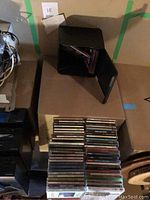 CDs stacked in two piles alongside black plastic DVD holder on cardboard box.