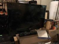 LG 32 inch LCD flatscreen TV with base stand placed on a box in a storage area.