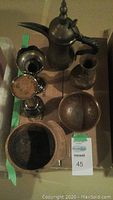 Top view of the lot shows wooden bowls, metal coffee pot, goblet, and small vase placed on a cardboard box.