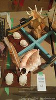 Overview of multiple sailboat and seashell decorative items arranged on a table, showing wooden sailboats with sails and mounted seashells.