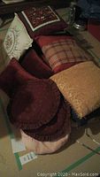 Assorted throw pillows including embroidered flowers, red ruffled pillows, a plaid pillow and gold damask pillow piled together