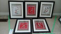 Group photo showing all five needlepoint pictures in black frames with floral and bird designs in various fabric colors.