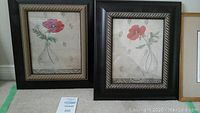 Two framed prints of red poppies in clear vases with black and gold rope-style frames, placed side by side on carpeted floor