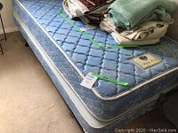 Side angle view of mattress and box spring with folded blankets on top, showing blue floral pattern and size tag.