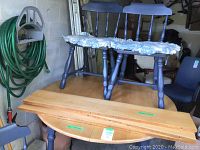 Photo shows round wooden kitchen table and chairs with blue paint and blue floral cushions.