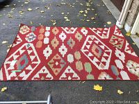Full view of the outdoor carpet showing its pattern and condition, laid flat on pavement with some leaves around.