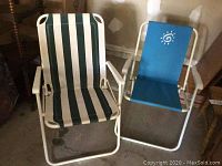 Two folding outdoor chairs, one with green and white striped fabric, the other with blue fabric and a sun design on the back.