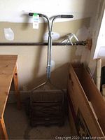 Push reel lawn mower upright, showing metal handlebar and part of reel blades assembly.