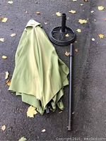 Photo showing the folded green umbrella canopy and the detached umbrella pole laid out on the ground.