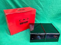 Red cardboard outer box and pair of black lacquered wooden cigar boxes placed side by side on green background