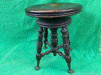 Side view of antique wooden swivel piano stool showing turned legs and metal claw feet