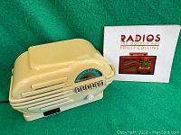 Cream colored Thomas Collectors Edition radio cassette player with five push buttons and tuning dial next to a book on bakelite radios.