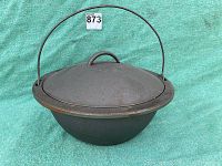 Front view of a round cast iron cooking pot with lid and tall bail handle, showing shape and condition.