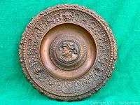 Full front view of round bronzed charger on green felt background