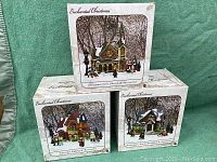 Photo showing three original boxes of Enchanted Christmas lighted houses: Christmas Cove Church, Victoria's Bakery, and Snowman Hill & Townshop.