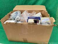 Front view of large cardboard box filled with assorted trading cards in plastic bags and boxes.