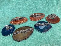 Top-down view of 6 polished agate slices each mounted with miniature metal trains and one prospector sculpture on green felt background.