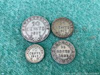 Four Newfoundland antique silver coins (50, 25, 20, 10 cents) displayed on a green cloth.