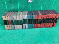 Full side view of 23 vintage hardcover books arranged in a row on green fabric backdrop.