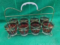Front view of 8 vintage glasses in gold-tone metal carrier with white handle.
