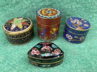 Four vintage cloisonne enamel trinket boxes together on green cloth background showing varied shapes and motifs.