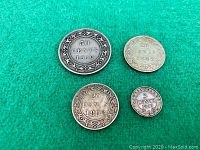 Four antique Newfoundland silver coins arranged on green felt, showing denominations and dates.
