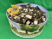 Large collection of assorted metal figure-shaped cookie cutters inside a Winnie the Pooh themed cylindrical hat box with rope handles and colorful outdoor nature illustrations.