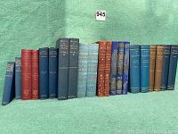 Books lined up on green fabric background showing variety of titles and colors in collection.
