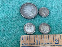 Four antique silver coins from Newfoundland displaying portraits of British monarchs with a ruler for scale.
