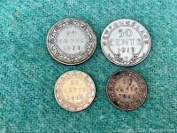 Four Newfoundland silver coins in varying conditions placed on green felt for display, two 50 cent and two 20 cent pieces.