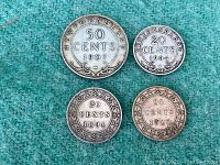 Four antique silver Newfoundland coins displayed on a green cloth. Includes two 20 cents coins from 1894 and 1900, one 20 cents from 1904, and one 50 cents from 1907.