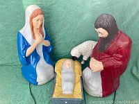 Front view of Mary, Joseph, Jesus in manger, and sheep figurines against a green background.