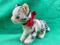 Front and side view of the vintage Steiff mohair kitten plush showing fur texture, red bow, and button with tag on the ear.