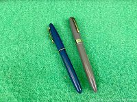 Two vintage fountain pens placed on green surface, showing the full pens.