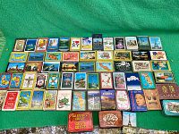 Full display of 49 vintage souvenir playing card decks with various travel themes laid out on green surface.