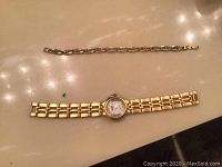 Photo showing a gold-tone women's watch and a matching bracelet with linked chain designs and stones on a surface.